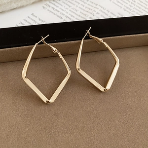 Macro detail of geometric rhombus drop earrings in polished gold metal on a display stand
