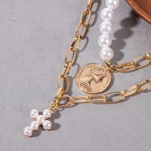 Close-up of double-layered gold necklace with baroque pearls, cross and coin pendants
