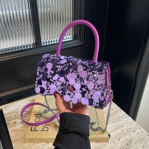 Detail of purple sequin handbag with silver chain strap and top handle on a book