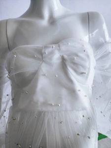 Detail of white mesh maternity gown featuring delicate pearl beads and soft tulle texture