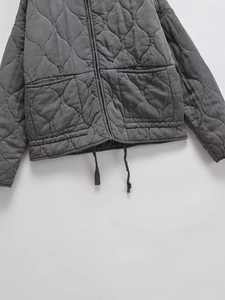 Detail of grey quilted jacket featuring onion stitching, zipper, and drawstring hem
