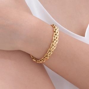 Close-up of a wide golden stainless steel watch-style link bracelet on a model wrist