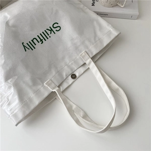 Transparent PVC and white canvas tote bag with green Skillfully text in a minimalist setting