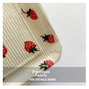 Close-up of premium beige corduroy fabric featuring cute red strawberry embroidery detail