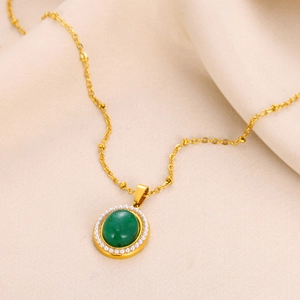 Detail of vintage gold necklace featuring a large emerald gemstone and pearl bezel