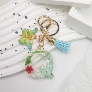 Detail of resin letter Q keychain with dried flowers, butterfly charm, and blue tassel
