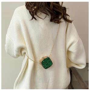 Detail of green sequin mini bag with gold chain strap on a knit sweater backdrop