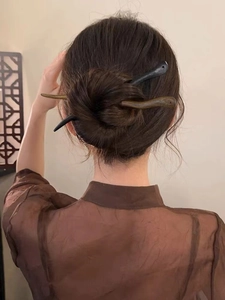 Détail de deux pics à cheveux en bois de santal marron et noir dans un chignon