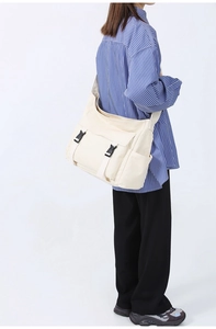 Vue latérale du sac bandoulière en toile beige avec boucles noires porté par un mannequin