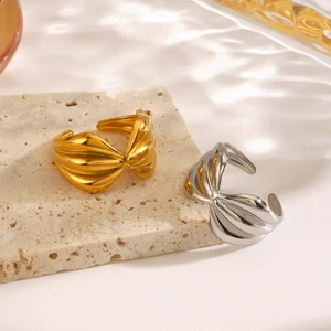 Polished 18K gold and silver bow twist open rings displayed on stone with water ripple shadow