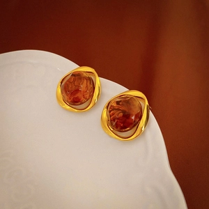 Close-up of vintage resin earrings featuring amber stones set in irregular gold metal frames