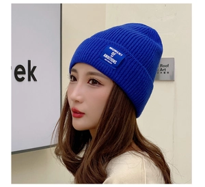 Detail of blue knit beanie featuring a white square woven label with blue letter embroidery
