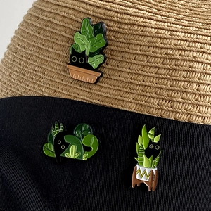 Detailed view of black cat and green plant enamel pins decorated on a stylish straw hat
