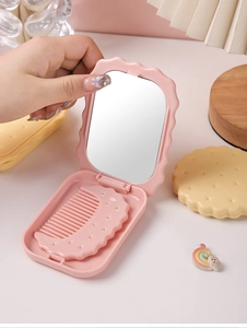 Pink biscuit-shaped compact mirror with a fold-out comb held in hand for detail view