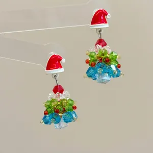 Macro detail of handmade beaded Christmas tree earrings with a festive red Santa hat stud