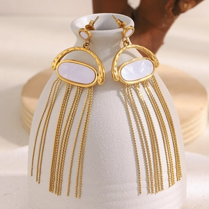 Détails des boucles d'oreilles coquillage doré avec pompons sur un vase en céramique
