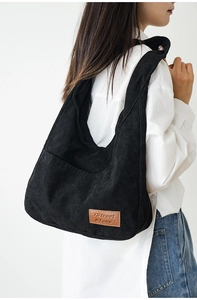 Detailed close-up of a black corduroy hobo shoulder bag with a brown leather logo tag