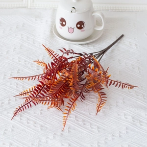 Detail of artificial orange fern leaf stem with autumn tones on white textured surface