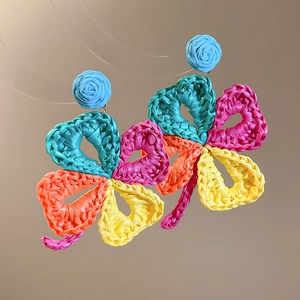 Detail of colorful woven raffia flower earrings featuring blue rose studs and heart petals