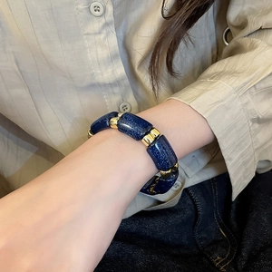 Detail of blue and gold acrylic geometric bracelet worn by model in casual home setting