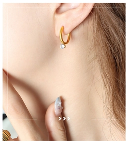 Detailed close-up of a gold hoop earring with a sparkling cubic zirconia stone on a model