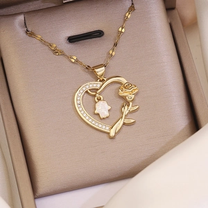 Macro view of gold-plated heart necklace with rose flower and Hamsa Hand pendant in a box