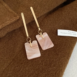 Detail of long geometric earrings with gold bars and pink marble resin pendants