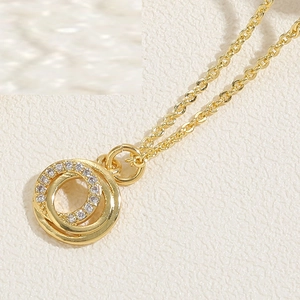 Close-up of interlocking circular gold pendants with zircon paving on textured background
