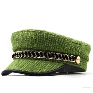 Detail of tweed newsboy cap in green with black leather brim and golden chain trim