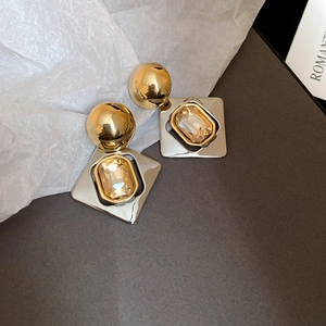 Détail de boucles d'oreilles géométriques bicolores serties de cristaux champagne