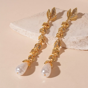 Detail view of long gold leaf earrings with rhinestones and a baroque pearl drop