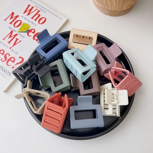 Top view of twelve colorful matte square hair claws arranged on a black decorative plate
