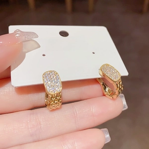 Detail von Goldohrringen mit Kettengliedern und Zirkonia auf einer weißen Karte