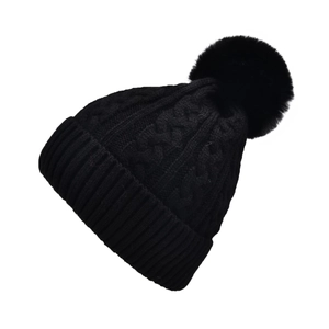 Detail of black cable knit beanie showing thick texture and fluffy faux fur pom-pom