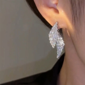 Luxury silver stud earrings with geometric diamond wings shown on a model's ear
