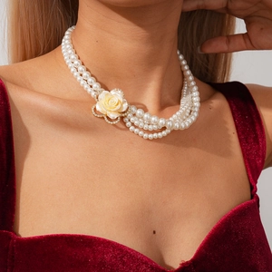 Dettaglio di collana di perle multistrato con rosa in resina gialla su abito di velluto