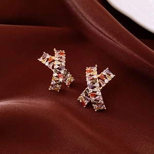 Macro shot of X-shaped gold earrings with colorful rectangular zircons on silk