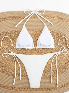 Detailed flat lay of white halter bikini set with a golden starfish buckle on straw mat