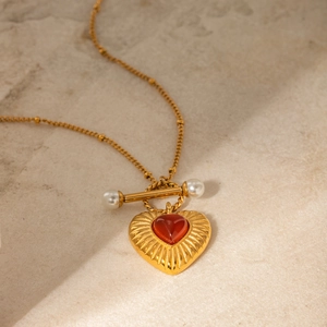 Detail of 18k gold heart necklace with red agate stone and pearl T-bar toggle closure