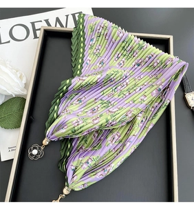 Detail of pleated silk scarf with floral pattern and pearl flower pendant on a tray