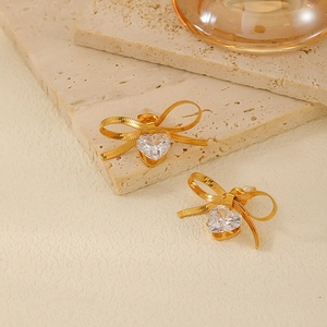 Close-up of golden bow earrings with heart-shaped crystal on a natural stone base
