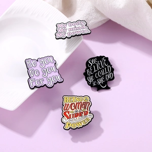 Détail de quatre épingles en émail coloré avec phrases de motivation sur fond violet