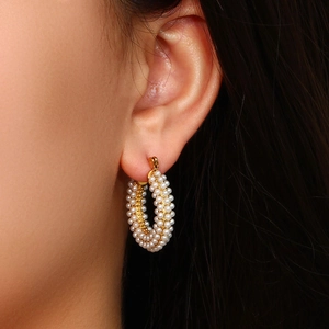 Close-up of gold plated hoop earrings with white pearls worn by a female model
