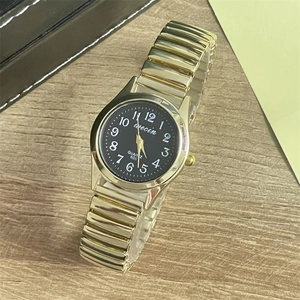 Detail of gold elastic steel band and black quartz watch face with luminous numbers