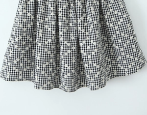 Close-up of black and white plaid dress with intricate white flower embroidery detail