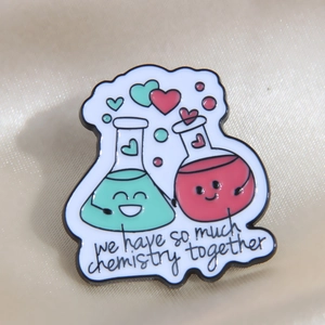 Macro shot of chemistry flask enamel pins with text on elegant beige silk fabric