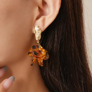 Close-up of golden hammered metal earrings with amber resin flower drop on a model