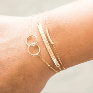 Detailed view of three gold minimalist bracelets with interlocking rings and engraving