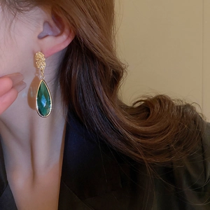 Close-up of vintage emerald green waterdrop earring on model with golden textured stud