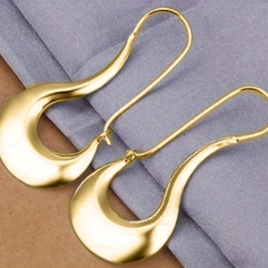 Detail of golden irregular curved drop earrings resting on light purple fabric texture